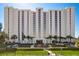 Modern condo building with a manicured lawn, palm trees, and parking spaces at 2425 Gulf Of Mexico Dr # 14B, Longboat Key, FL 34228