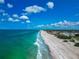 Expansive white sand beach meets turquoise water under a bright blue sky with fluffy white clouds in this aerial view at 3630 Gulf Of Mexico Dr # 202, Longboat Key, FL 34228