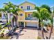 Bright yellow two-story home with a balcony, palm trees, and a paved driveway leading to the garage at 145 50Th St, Holmes Beach, FL 34217