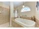 Relaxing bathroom featuring a soaking tub, tiled surround, glass shower, and arched window at 5359 90Th Avenue E Cir, Parrish, FL 34219