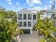 Front elevation of a 3 story white home with 2 levels of balconies, a dark garage door, and landscaping at 109 Palmetto Ave, Anna Maria, FL 34216