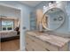 Bright bathroom featuring a wood vanity with granite countertop, stylish round mirror, and direct bedroom access at 4120 51St W Dr, Bradenton, FL 34210
