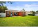 Expansive backyard showcasing lush greenery, a brick patio with outdoor seating, and a vibrant orange home exterior at 4194 Banbury Cir, Parrish, FL 34219