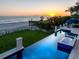 Luxury beachfront home with an infinity pool overlooking the ocean at sunset with manicured lawn at 845 Longboat Club Rd, Longboat Key, FL 34228
