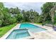 Stunning pool and spa with a travertine patio, mature landscaping, and lush green grass at 8963 Fishermens Bay Dr, Sarasota, FL 34231