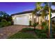 Dusk view of a charming home featuring lush landscaping, a brick driveway, and a two-car garage at 6791 Alstead Cir, Bradenton, FL 34202