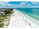 Aerial view of a picturesque sandy beach with clear turquoise water and scattered beachgoers under a partly cloudy sky at 5806 Gulf Dr # 201, Holmes Beach, FL 34217