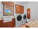 Well-lit laundry room with granite countertops, wooden cabinetry, and modern washer and dryer units at 7025 Saddle Creek Cir, Sarasota, FL 34241