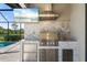 Outdoor kitchen area with stainless steel appliances, stone countertops, and a mounted television at 15316 Shady Palms Ln, Nokomis, FL 34275