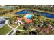 Aerial view of clubhouse with a red tile roof, tropical landscaping, pool, and a serene lake view at 3218 Big Sky Way, Bradenton, FL 34211