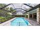 A swimming pool with an enclosure and brick columns that support the roof with lush landscaping in the background at 6107 Misty Oaks St, Sarasota, FL 34243