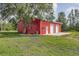 Red outbuilding/barn featuring two garage doors, a service door, and lush green landscape at 3045 Logue Rd, Myakka City, FL 34251