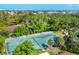 Aerial shot of a well-maintained tennis court in a lush neighborhood with mature trees and palms at 6832 Woodwind Dr # 53, Sarasota, FL 34231