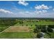 Wide aerial shot showing the property layout with pastures, ponds, neighboring homes, and extensive greenery under a partly cloudy sky at 26147 L And J Rd, Myakka City, FL 34251