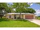 Inviting single-story house with a lush green lawn, mature trees, metal roof, and a two-car garage at 26147 L And J Rd, Myakka City, FL 34251