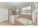 Bathroom showcases a tiled soaking tub and glass shower with travertine tile and white cabinets at 138 Toscavilla Blvd, Nokomis, FL 34275
