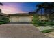 Evening view of a home featuring a brick driveway, manicured landscaping, and three-car garage at 138 Toscavilla Blvd, Nokomis, FL 34275