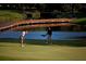 Golfers on a meticulously maintained golf course, featuring a wooden bridge, a pond, and rolling green hills in the background at 140 Sugar Mill Dr, Osprey, FL 34229