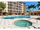 Resort-style pool and hot tub area, with an expansive deck and comfortable seating beneath shade structures, under a clear blue sky at 1921 Monte Carlo Dr # 302, Sarasota, FL 34231