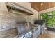 Outdoor kitchen with stainless steel grill and pizza oven with stone backsplash and overhead exhaust hood at 303 Cockle Shell Loop, Apollo Beach, FL 33572