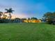 Expansive backyard with lush green lawn, swaying palm trees, outdoor seating, and a serene sunset sky at 355 Shore Dr, Ellenton, FL 34222