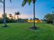 Expansive backyard with lush green lawn, swaying palm trees, outdoor seating, and a serene sunset sky at 355 Shore Dr, Ellenton, FL 34222
