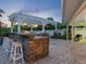 Outdoor kitchen with bar seating, a stone counter, white pergola, and brick patio, perfect for entertaining at 355 Shore Dr, Ellenton, FL 34222