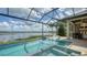 Screened pool area with a spa, lounge chairs, and an outdoor kitchen, offering a luxurious lakeside experience at 7665 Haddington Cv, Bradenton, FL 34202