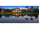 Waterfront home at twilight with lush landscaping, a pool, and a tranquil reflection in the water at 7665 Haddington Cv, Lakewood Ranch, FL 34202