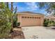 A well-maintained two-car garage with a light peach door, complemented by mature landscaping and a concrete driveway at 6352 Robin Cv, Lakewood Ranch, FL 34202