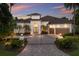 Elegant single-story home featuring a gated entrance, arched entryway, two-car garage, and lush tropical landscaping at dusk at 7211 Pasadena Gln, Lakewood Ranch, FL 34202