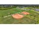 Aerial shot of well-maintained sports fields, including baseball and soccer fields, surrounded by lush greenery and palm trees at 10254 Morning Mist Ln, Sarasota, FL 34241