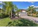 Beautifully landscaped home featuring a paver driveway, lush green lawn, and complemented by mature palm trees and shrubs at 19023 Mangieri St, Venice, FL 34293