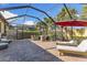 Screened-in patio featuring brick pavers, lounge chairs, dining set, grill, and sun umbrella with lush greenery visible around the area at 19023 Mangieri St, Venice, FL 34293