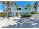 Charming two-story beach home with light blue siding, a yellow door, and lush palm trees at 733 Holly Rd, Anna Maria, FL 34216