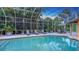 Screened pool and sun-deck with loungers, umbrella, manicured hedges and clear blue water at 1627 Peregrine Point Ct, Sarasota, FL 34231