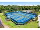 An eye-level view of tennis courts with blue borders, green and blue playing surfaces, with people playing tennis on a sunny day at 12261 Stuart Dr, Venice, FL 34293