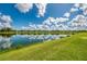 Scenic lakeside view with lush green lawn, blue sky, puffy white clouds, and waterfront homes in the distance at 6318 Rivo Lakes Blvd, Sarasota, FL 34241