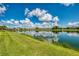 A serene lake view is captured with lush green grass leading to the water's edge, with homes visible in the distance at 6318 Rivo Lakes Blvd, Sarasota, FL 34241