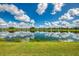 Scenic lake with reflections of a clear blue sky and scattered clouds, complemented by a vibrant green lawn and community homes at 6318 Rivo Lakes Blvd, Sarasota, FL 34241