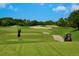 Golfer swinging on the lush green course with sand traps and a golf cart under a sunny, blue sky at 4374 Mirabella Cir, Bradenton, FL 34210