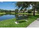 Scenic view of a pond with a black bench, grassy shoreline, and trees in a residential community at 4374 Mirabella Cir, Bradenton, FL 34210