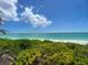 Serene beach view with lush greenery in the foreground, showcasing clear turquoise water and a bright blue sky with clouds at 5364 Salcano St, Sarasota, FL 34238