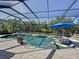 A beautiful screened-in pool and spa area with a blue umbrella, lounge chairs, and lush landscaping at 336 165Th Ne Ct, Bradenton, FL 34212