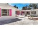 Charming single-story home featuring white exteriors, vibrant pink shutters, and a well-manicured, inviting entrance at 5572 Shadow Lawn Dr, Sarasota, FL 34242