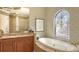 Elegant bathroom featuring a soaking tub under an arched window, dual sinks and a walk-in shower at 8832 Enclave Ct, Sarasota, FL 34238