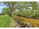 Waterfront backyard view with mature tree, landscape, and canal with rocky edge at 2115 9Th W Ave # 3D, Bradenton, FL 34205