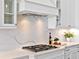 Close-up of the kitchen showcasing the sleek gas cooktop, custom range hood, and elegant marble backsplash at 16917 Clearlake Ave, Lakewood Ranch, FL 34202