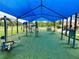 Outdoor gym area with varied exercise equipment under a blue canopy on a green turf surface in a park setting at 5702 Tangerine S Ave, Gulfport, FL 33707