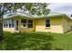 Bright yellow home with a green metal roof and a sunny enclosed porch, surrounded by a lush green lawn at 6114 68Th E Dr, Palmetto, FL 34221